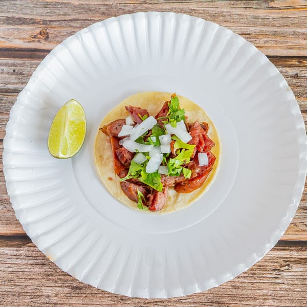 A Tap N Taco Mexican taco with meat, onions, and cilantro, served with a lime wedge.