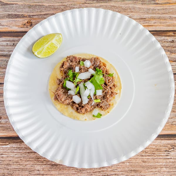 A Tap N Taco beef taco with onions and cilantro, served with a lime wedge on a white plate.