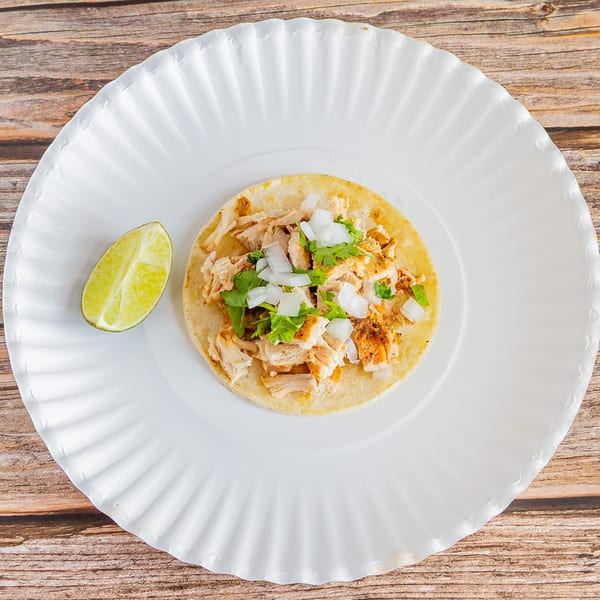 A Tap N Taco chicken taco with onions and cilantro, served with a lime wedge on a white plate.