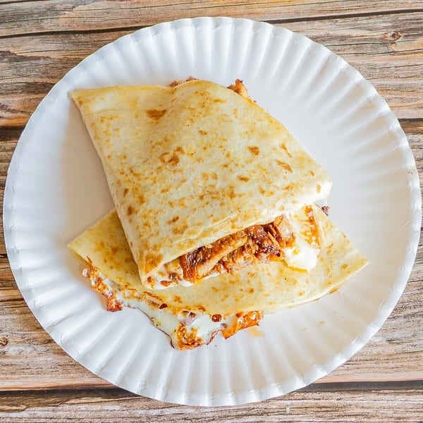 A Tap N Taco quesadilla, filled with meat and melted cheese, served on a white paper plate.