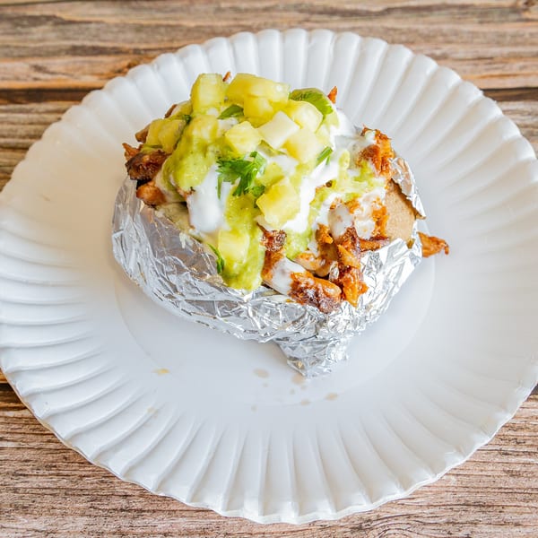 Tap N Taco's foil-wrapped baked potato topped with meat, guacamole, sour cream, and pineapple.