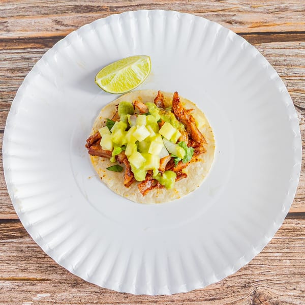 Tap N Taco's al pastor taco with pineapple and guacamole on a white paper plate.